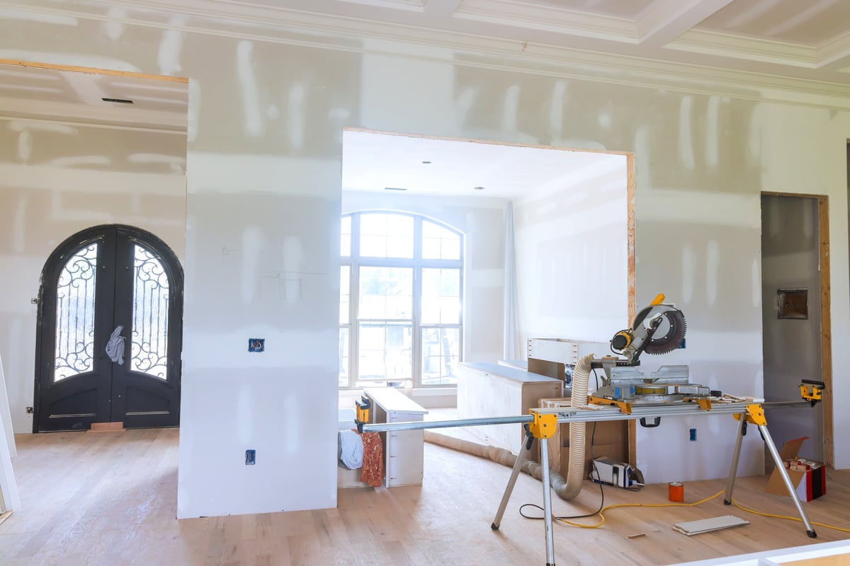 An empty living room mid-renovation, with unfinished walls, tools, and construction dust awaiting final cleanup