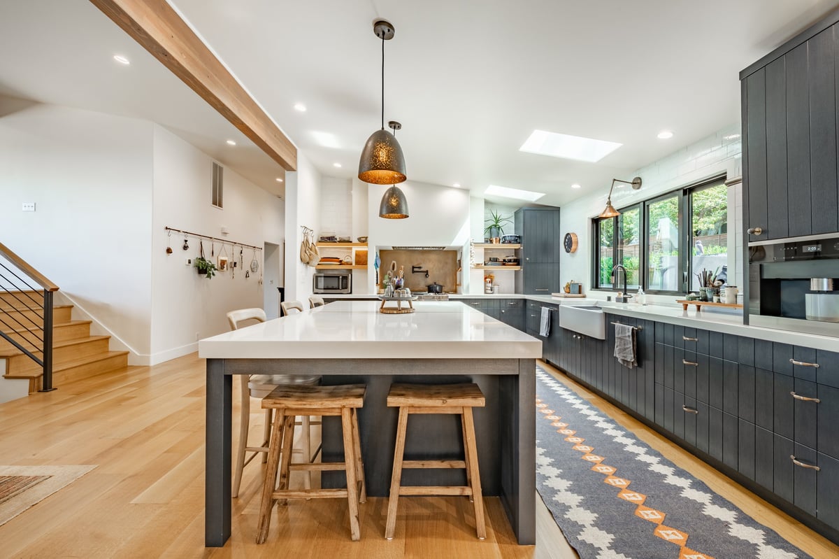 A clean modern kitchen with a large central island, pendant lights, and bright natural light